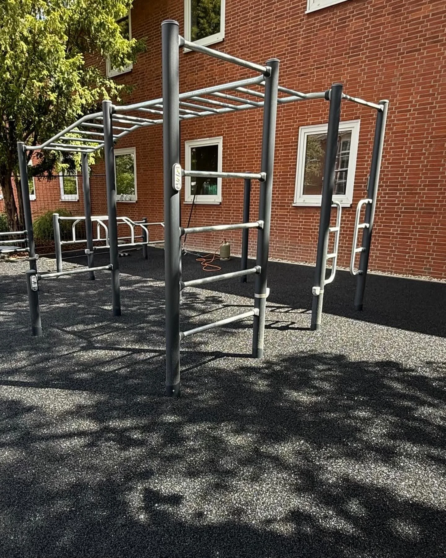 Calisthenics-Anlage auf schiefergrauer Fallschutzfläche vor einem Backsteingebäude