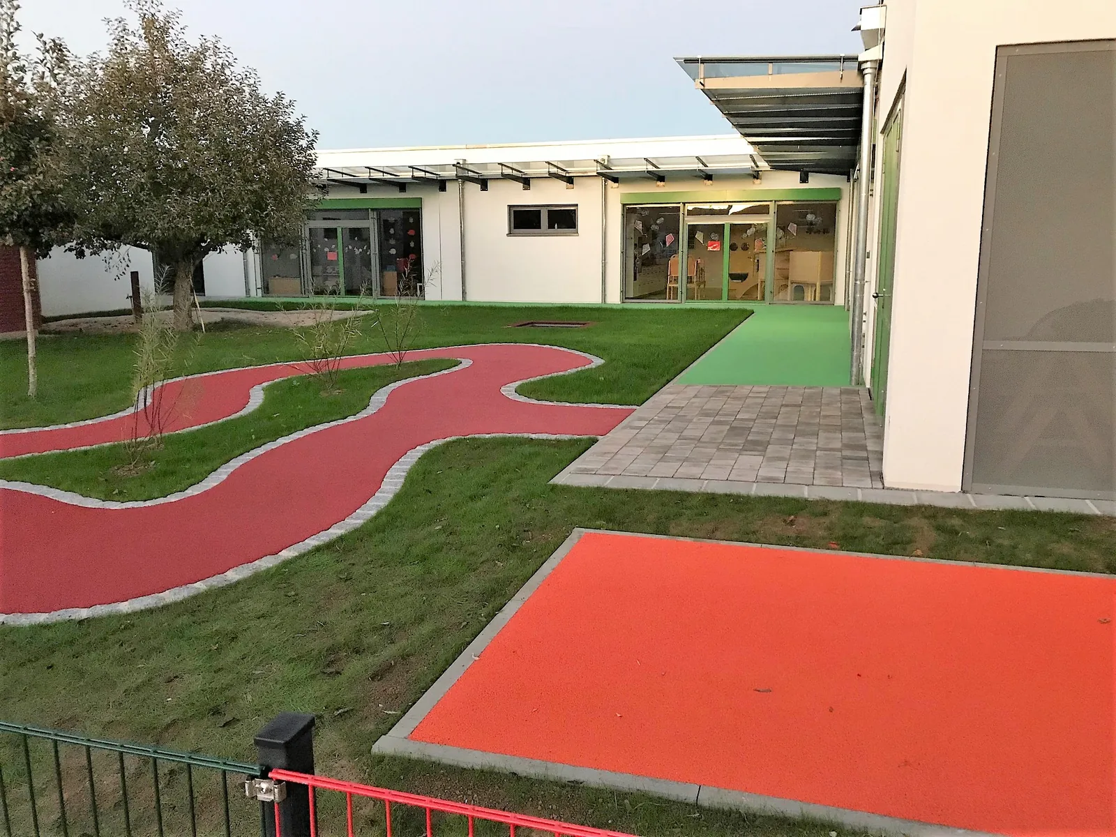 Frei geformte rote Fallschutzflächen und Wegeschleifen auf dem Außengelände einer Kindertagesstätte