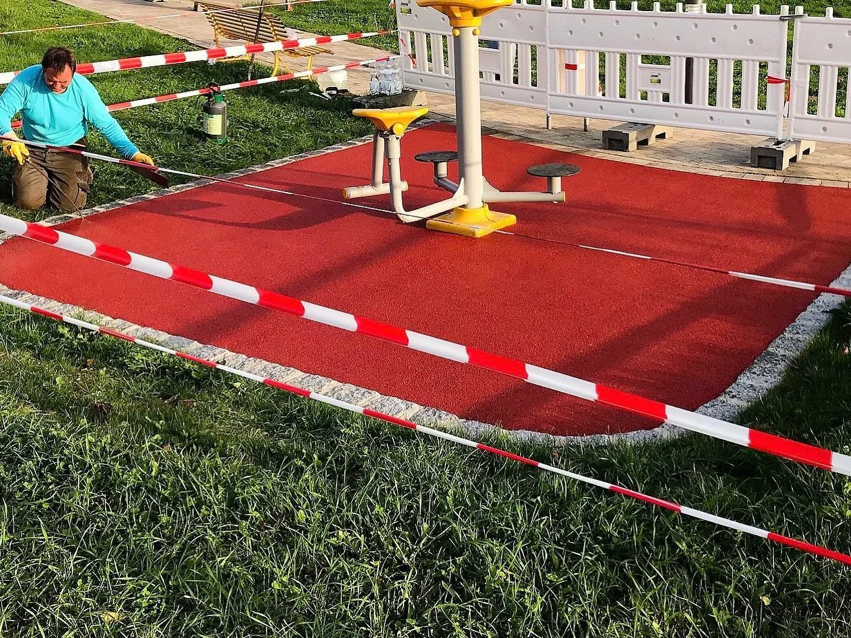 Ziegelrote Fallschutzfläche unter einem Outdoor-Fitnessgerät, frisch eingebaut und mit Absperrband gesichert