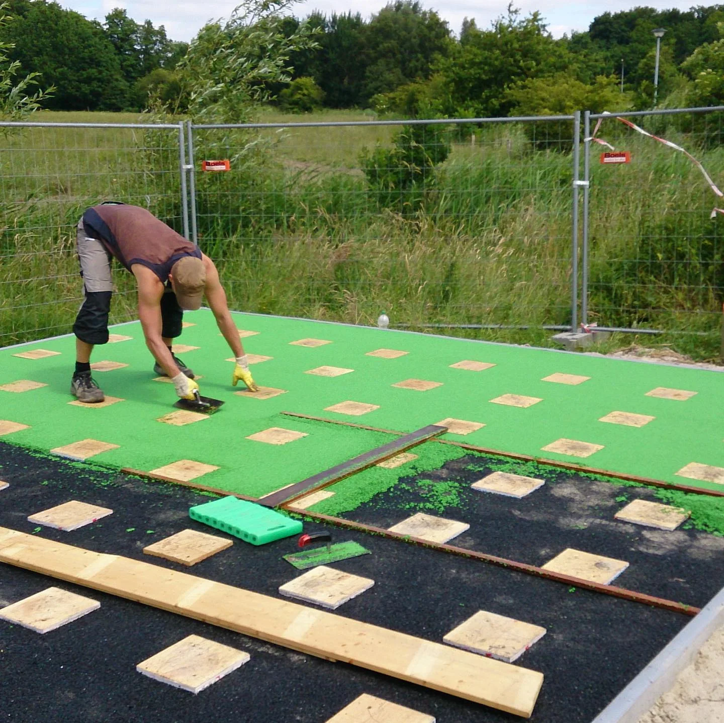 Mitarbeiter bei der Arbeit an einer maigrünen Fallschutzfläche mit Rasterplatten