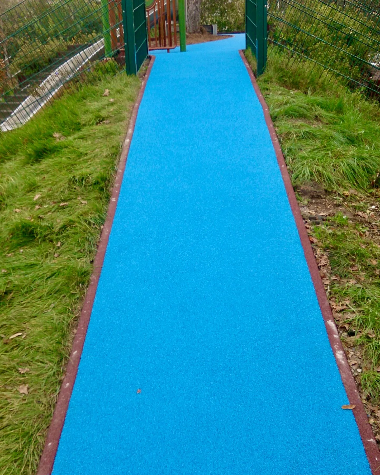 Himmelblauer Gehweg mit ziegelroter Einfassung als Zugang zum Spielplatz