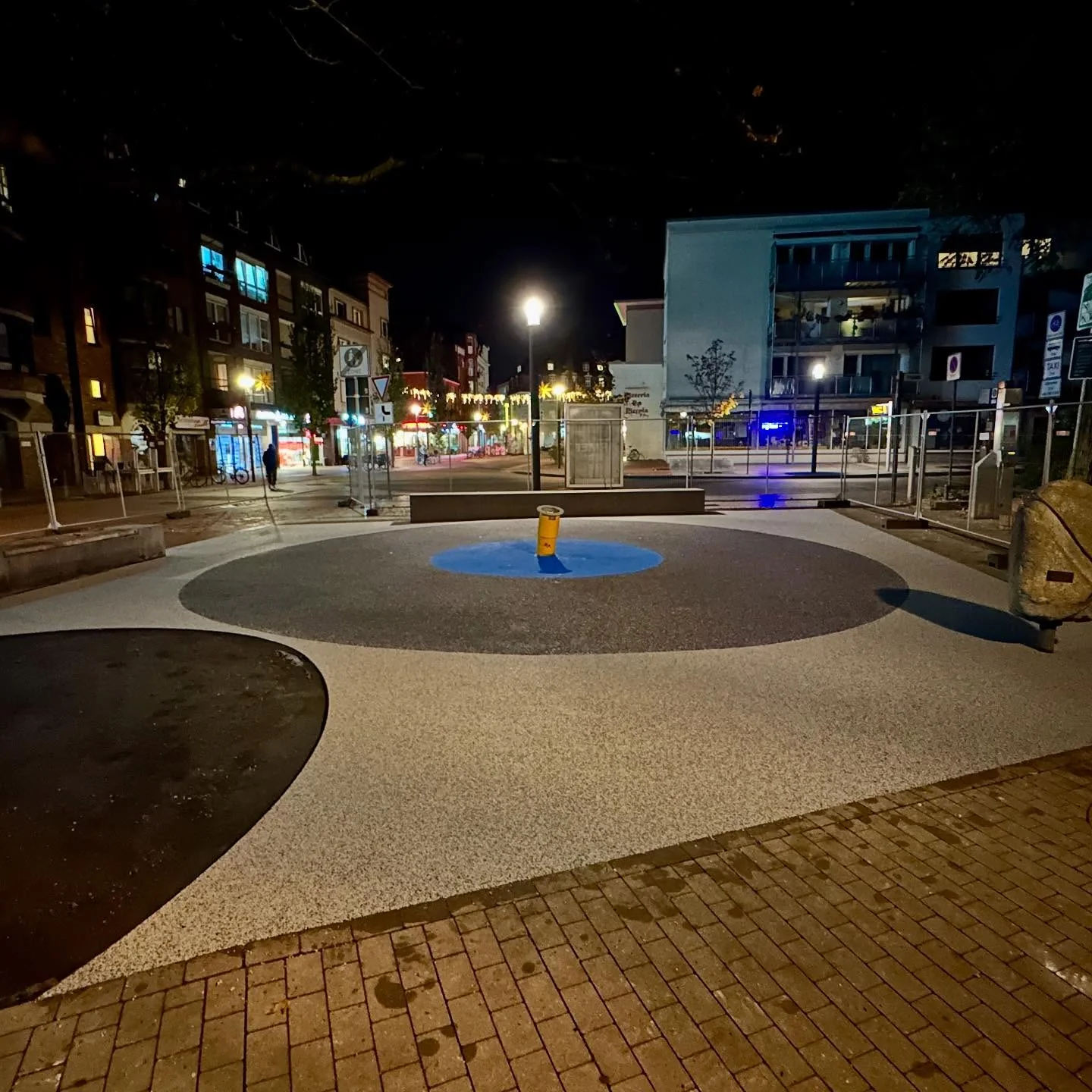 Beleuchtete Spielfläche bei Nacht mit lichtgrauem Belag und blauem Kreis